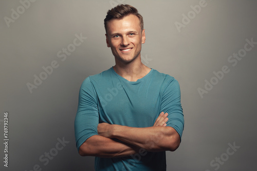 Male beauty concept. Portrait of smiling 30-year-old man standing over gray background with crossed hands. Classic style. Wavy glossy blond hair. Copy-space. Studio shot photo