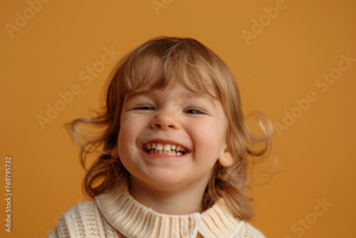 Laughing toddler with blonde curly hair on a mustard yellow background