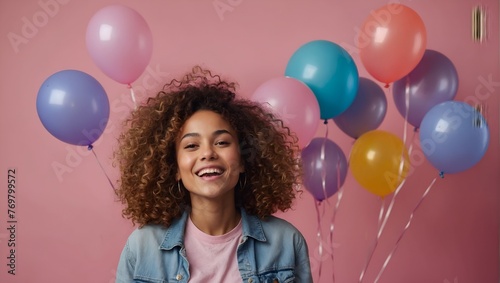 Beautiful mixed race with curly haired young woman rejoicing, posing against pink colored background with colorful air balls. Birthday party, anniversary, celebration, events concept