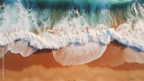 Aerial view of the ocean waves crashing against brown sand, creating dynamic patterns and textures. 