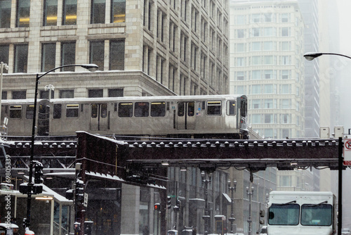 Subway leaving an eleveted station, goes through buildings in downtown Chicago while it's snowing