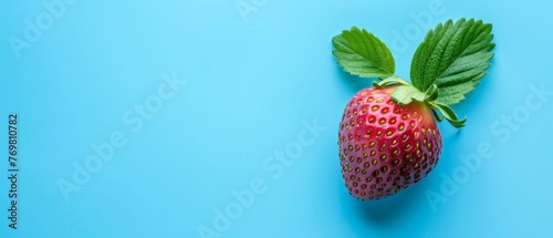   A strawberry with a green leaf on a blue background with a shadow from above