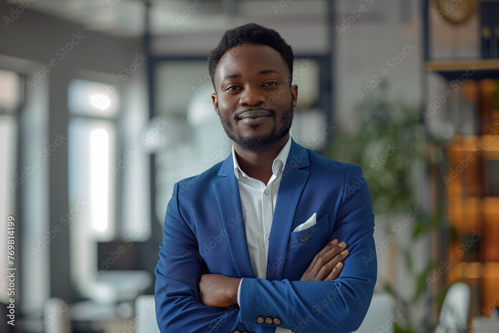 Portrait of a Confident Young African American Businessman Standing in Office in a Blue Business Suit. Successful Corporate Manager Posing for Camera with Crossed Arms, Smiling Cheerfully Portrait of a Confident Young African American Businessman Standing in Office in a Blue Business Suit. Successful Corporate Manager Posing for Camera with Crossed Arms, Smiling Cheerfully