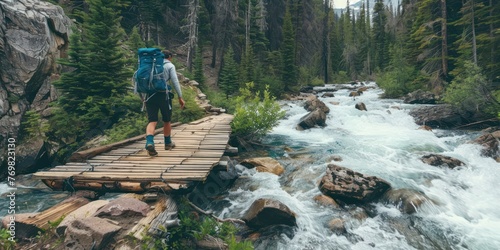 A hiker crossing a wooden bridge over a rushing mountain stream. 