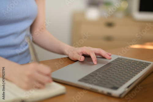 A woman is typing on a laptop while writing in a notebook