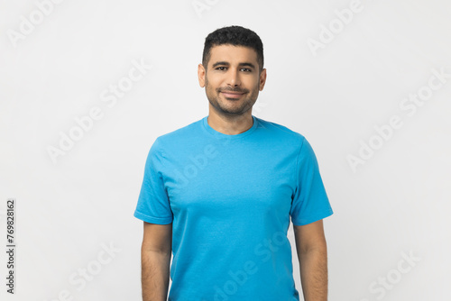 Portrait of happy smiling satisfied unshaven man wearing blue T- shirt standing looking at camera, expressing positive emotions. Indoor studio shot isolated on gray background. © khosrork