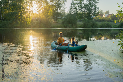 family rides in a rubber boat on the lake, boy and girl with dad, dad with daughter and son, sunset
