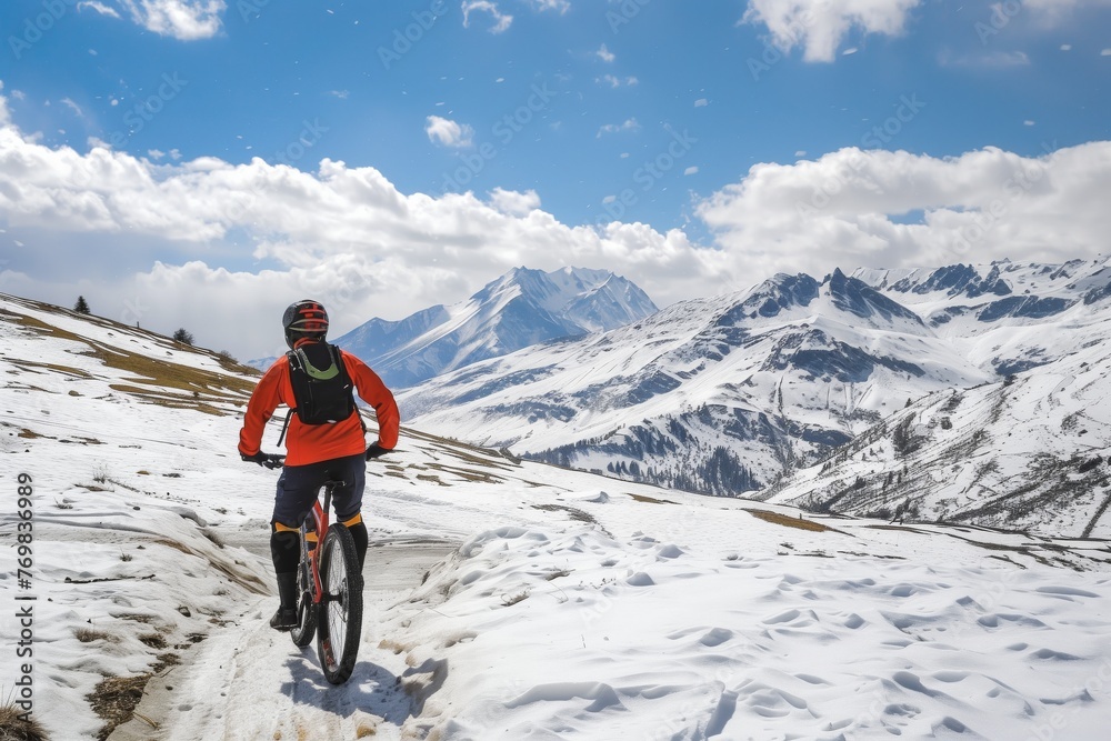 mountain biker on snowy trail with peaks in distance
