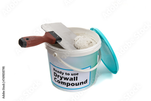 An open plastic pail of drywall joint compound, referred to as mud in a pail with a generic fake label with a wide drywall joint knife isolated on white