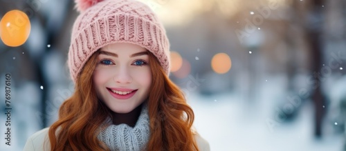 A woman in a pink knit cap and scarf is smiling happily in the snow, her eyelashes coated in snowflakes. The bright electric blue background adds to the fun winter scene