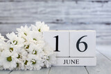 White wood calendar blocks with the date June 16th and white daisies. Selective focus with blurred background. 