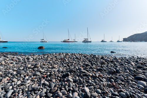 Fototapeta Naklejka Na Ścianę i Meble -  View with boats of the coast of Akrotiri and the black sand beach that is known locally as Mesa Pigadia beach. Greek Islands, Santorini, European Vacation