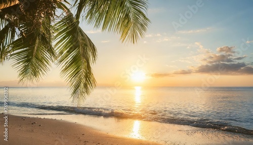 a summer vacation holiday background of a tropical beach and blue sea at sunset with the sun on the horizon and green palm tree leaves
