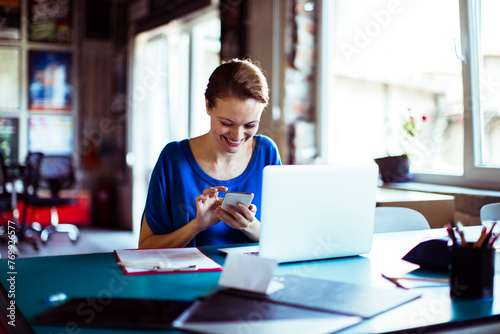 Smiling young woman using smartphone at her office desk photo