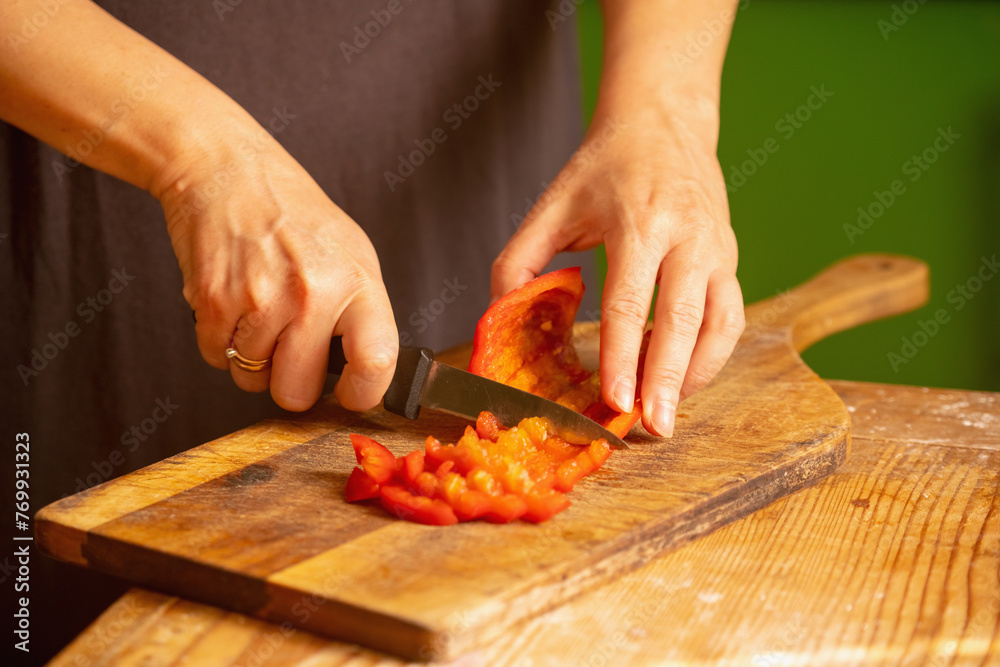 Italian bread and ingredients - parmesan, olive oil, tomato, spice and herbs. Portrait of chef's hands cuts red pepper slices on a pizza. Horizontal image.