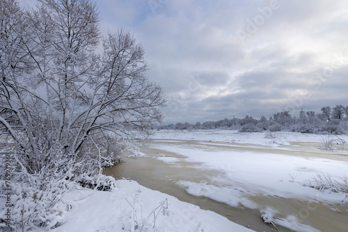 Classic winter landscape with a river and a tree in the foreground. Perspective and composition in landscape