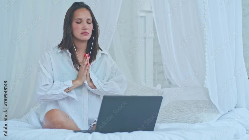 Young adult pretty woman breathing with headphones meditating on bed listening music to relax or audio podcast doing yoga meditation. Young adult pretty woman breathing with headphones meditating on bed listening music to relax or audio podcast doing yoga meditation.