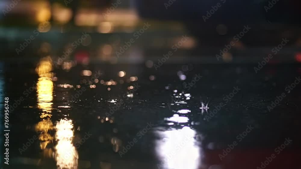 Atmospheric video of rainstorm in a night city. Heavy rain and splashes puddles taken from low point. Large drops break on the pavement in the light of street lamps. Slow motion