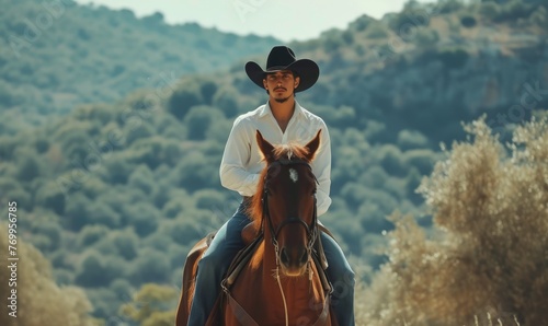 Handsome man wearing white shirt and dark hat with blue jeans and sitting on horse. Riding on obey horse in outdoor or ranch area. banner.