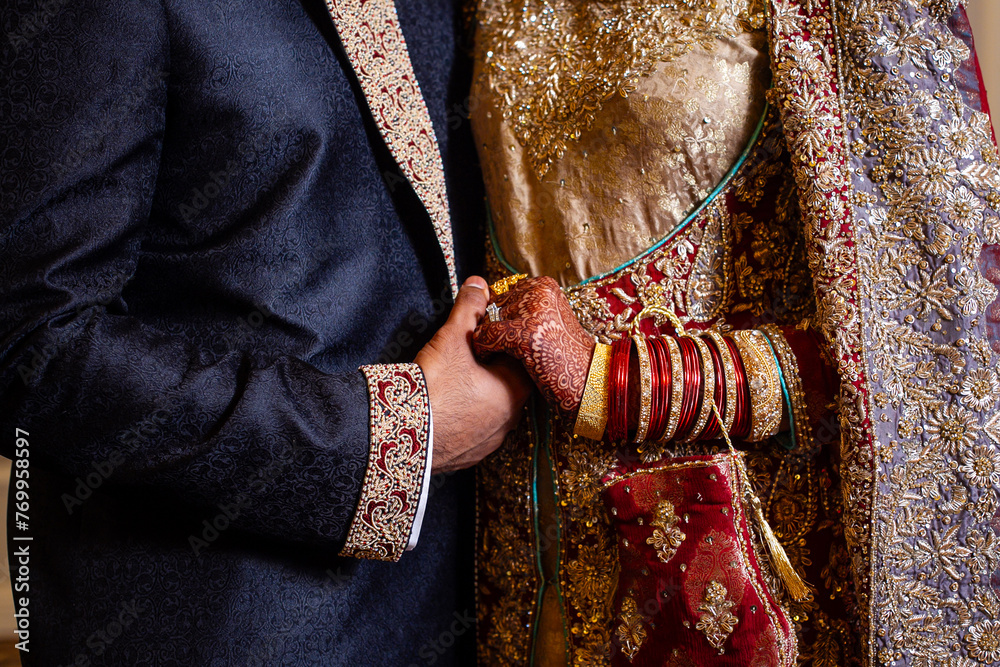 Muslim bride and groom in traditional garb hold hands on wedding day 