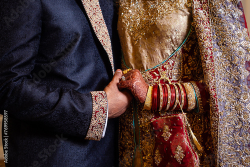 Muslim bride and groom in traditional garb hold hands on wedding day 