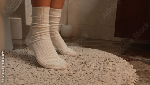 Girl puts on black lace panties while sitting on the toilet, female legs in white warm winter socks close-up