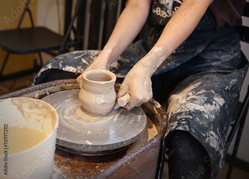 A woman works on a potter's wheel. Hands form a cup of wet clay on a potter's wheel. Artistic concept.