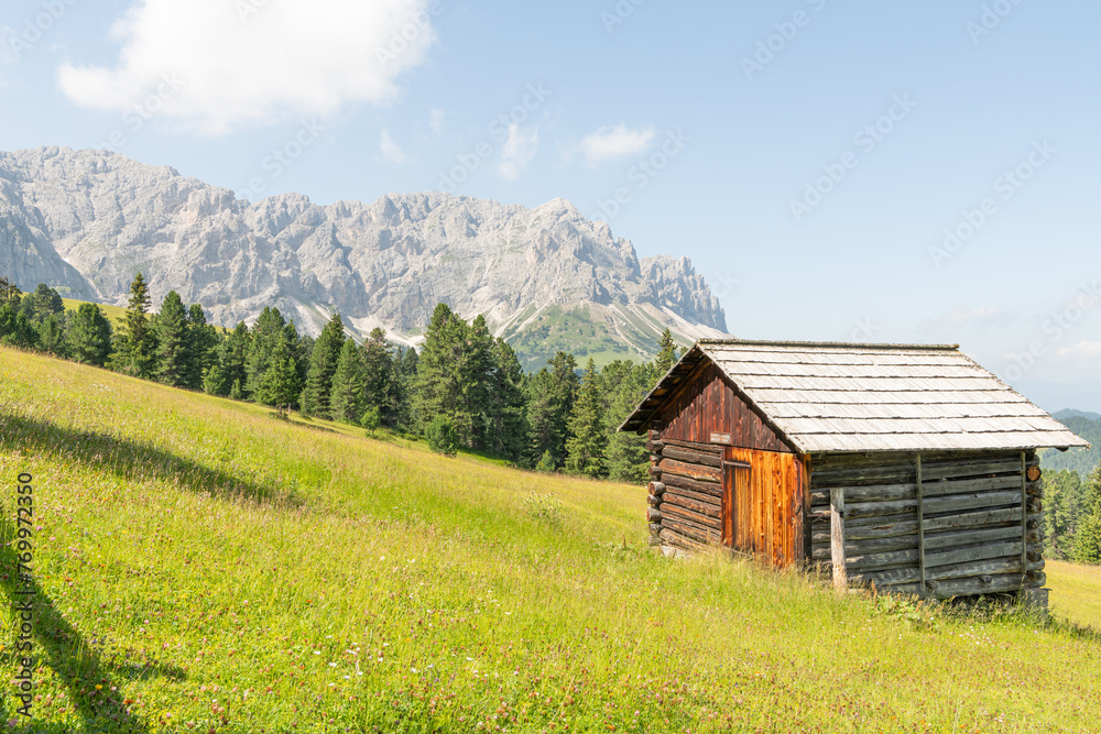 Beautiful summer view on a wooden mountain hut. Idyllic scenery, Alpine meadow in the foreground, rocky Italian mountains in the background. Sunny summer day. Villnöß, Villnöss Valley, South Tyrol. Beautiful summer view on a wooden mountain hut. Idyllic scenery, Alpine meadow in the foreground, rocky Italian mountains in the background. Sunny summer day. Villnöß, Villnöss Valley, South Tyrol.