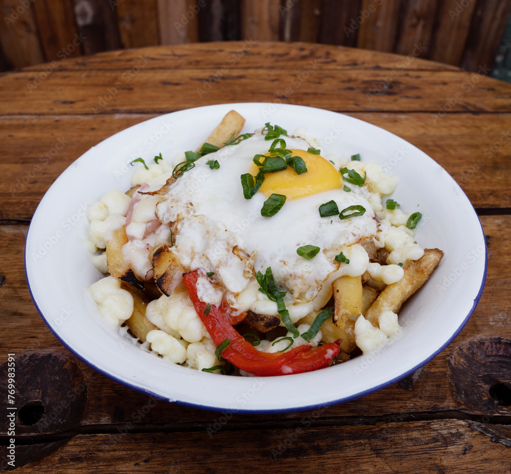 Closeup view of fried potatoes with melted cheese, chorizo, bell pepper, onion and a grilled egg in a white bowl on the wooden table. Closeup view of fried potatoes with melted cheese, chorizo, bell pepper, onion and a grilled egg in a white bowl on the wooden table.