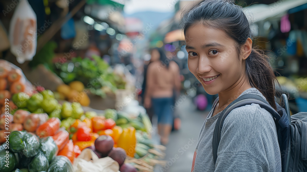 Young woman smiling at the camera in a street market with fresh vegetables in the foreground.