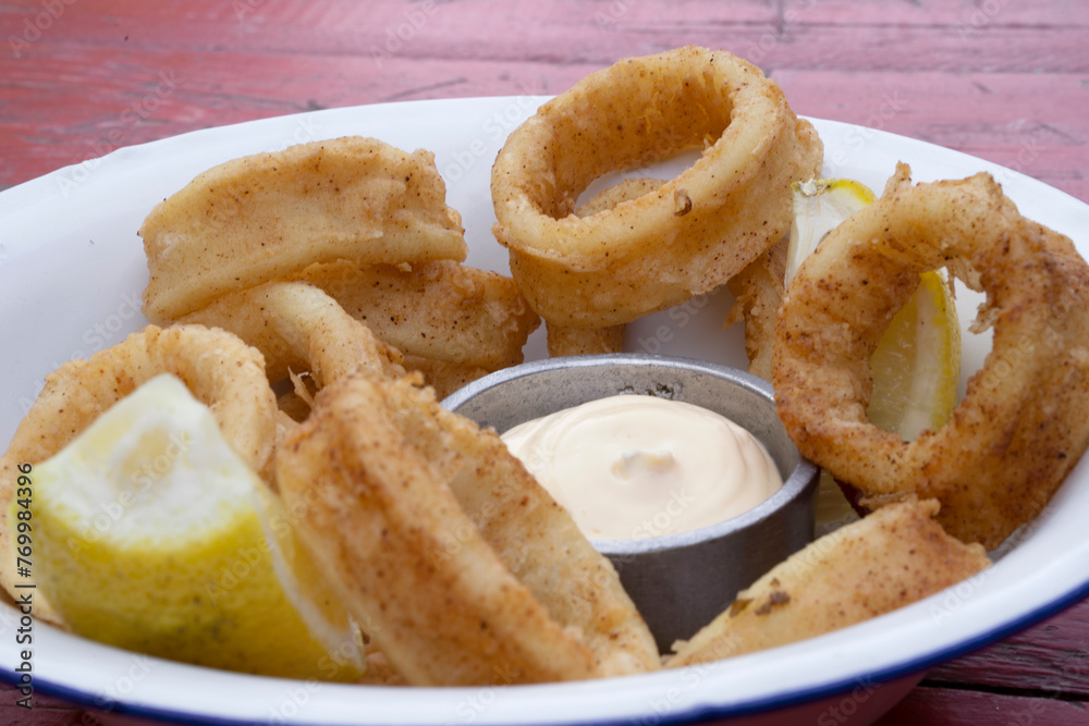 Fried seafood. Closeup view of delicious fried squid rings with lemon and a dipping sauce in a white bowl.	
