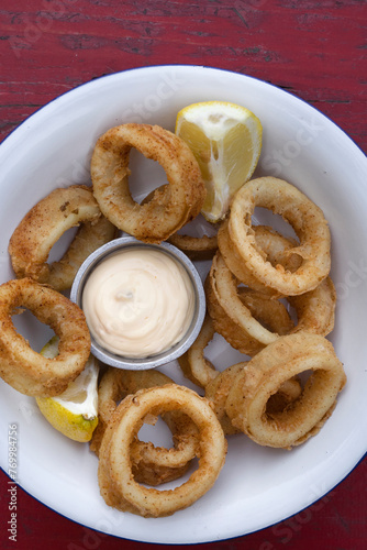 Fried seafood. Top view of delicious fried squid rings with lemon and a dipping sauce in a white bowl. 