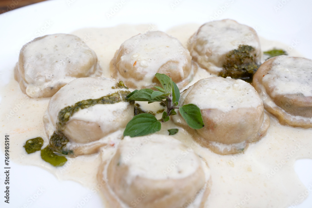 Italian food. Pasta. Closeup view of mozzarella cheese and ham sorrentinos with cream and pesto sauce, in a white dish. Italian food. Pasta. Closeup view of mozzarella cheese and ham sorrentinos with cream and pesto sauce, in a white dish.