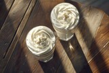 A mesmerizing aerial view captures two delectable milkshakes topped with frost, resting on a rustic wooden surface, exuding refreshment and delightful flavors.