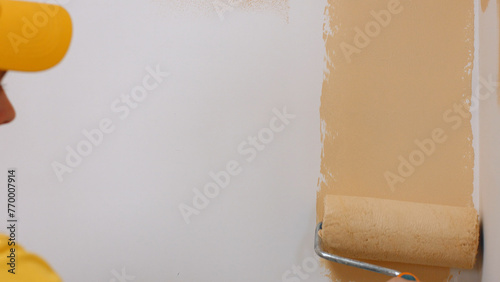 Painting the walls in the house. Builder paints white wall in beige color with a roller. © DenisProduction.com
