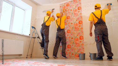 Brigade of craftsmen making renovation. Specialists wallpapering in the house. © DenisProduction.com