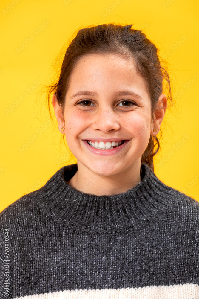 Portrait of a happy young girl with a bright smile, wearing a cozy sweater, set against a vivid yellow background Portrait of a happy young girl with a bright smile, wearing a cozy sweater, set against a vivid yellow background