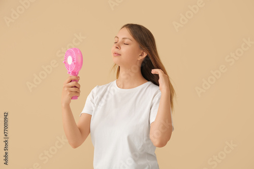 Beautiful young woman with handheld mini fan on beige background
