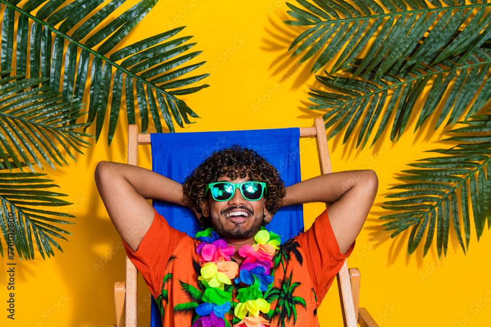 Portrait of satisfied guy wear hawaii print shirt in glasses lay on chair hold arms behind head isolated on yellow color background