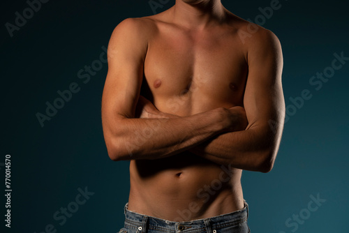 the torso of a young athletic guy with hands folded. concept: the male body after exercise and diet. men's health: shaved breasts on a dark background