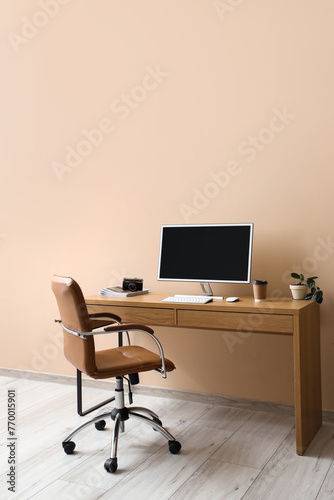Stylish workplace with modern computer and comfortable armchair near color wall