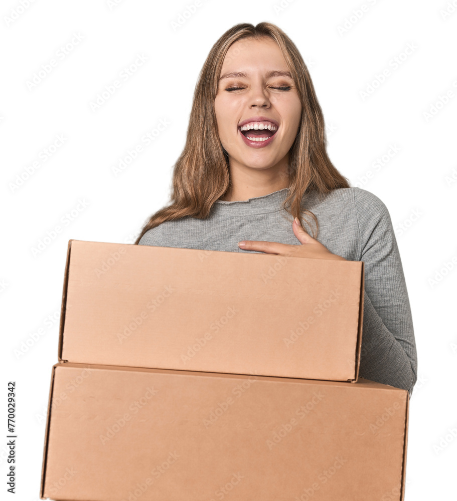 Blonde woman with cardboard boxes moving on studio backdrop laughs out loudly keeping hand on chest. Blonde woman with cardboard boxes moving on studio backdrop laughs out loudly keeping hand on chest.