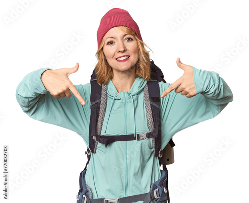 Middle-aged Caucasian woman with hiking gear points down with fingers, positive feeling.
