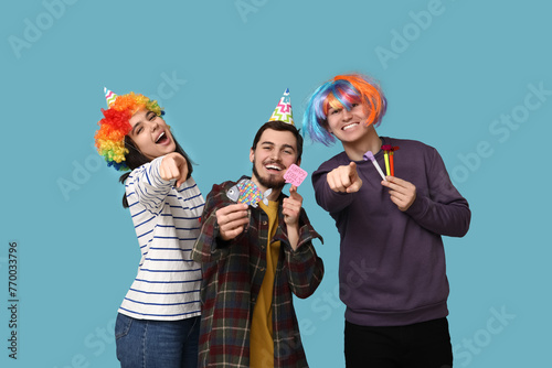 Young friends in funny disguise with whistles and paper stickers on blue background. April fool's day celebration