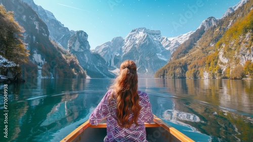  A woman sits in a boat amidst a body of water, surrounded by mountains with snow-capped peaks in the distance