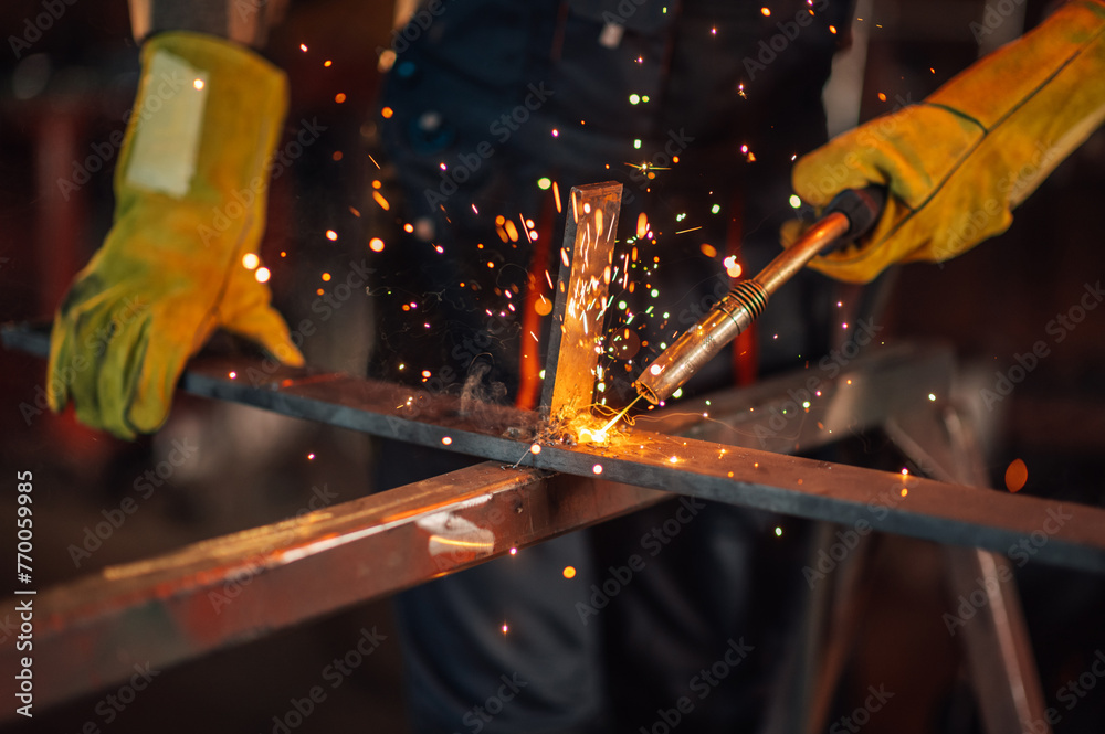 © Zamrznuti tonovi - Focus on yellow sparks flying all around while a worker welds metal.
