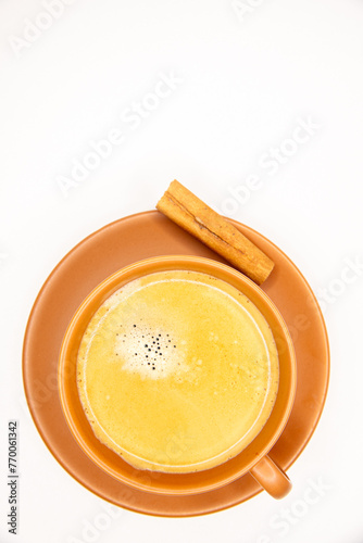 Xícara de café preto com espuma dourada, pires e xicara em terracota, bege, marrom, terra, rama de canela em fundo branco, espaço negativo para postagens.