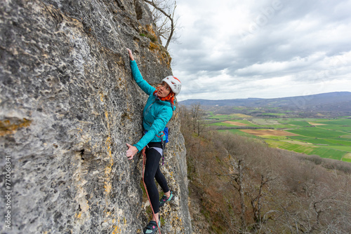A woman is climbing a rock wall wearing a blue jacket and a red hat. Concept of adventure and excitement as the woman conquers the challenging climb