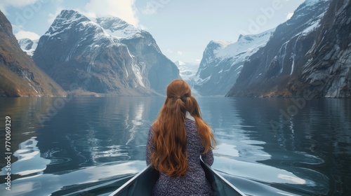  A woman with long, red hair sits in a boat amidst a snow-covered landscape, with majestic mountains reflected in the body of water behind her