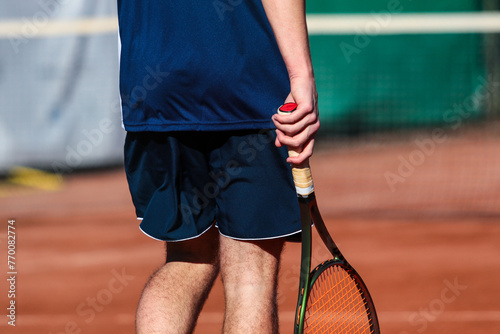 Close up of young boy with racket playing tennis on a clay court during a university tournament. the athlete is wearing a blue sports shirt. © Vamos Sports Prod